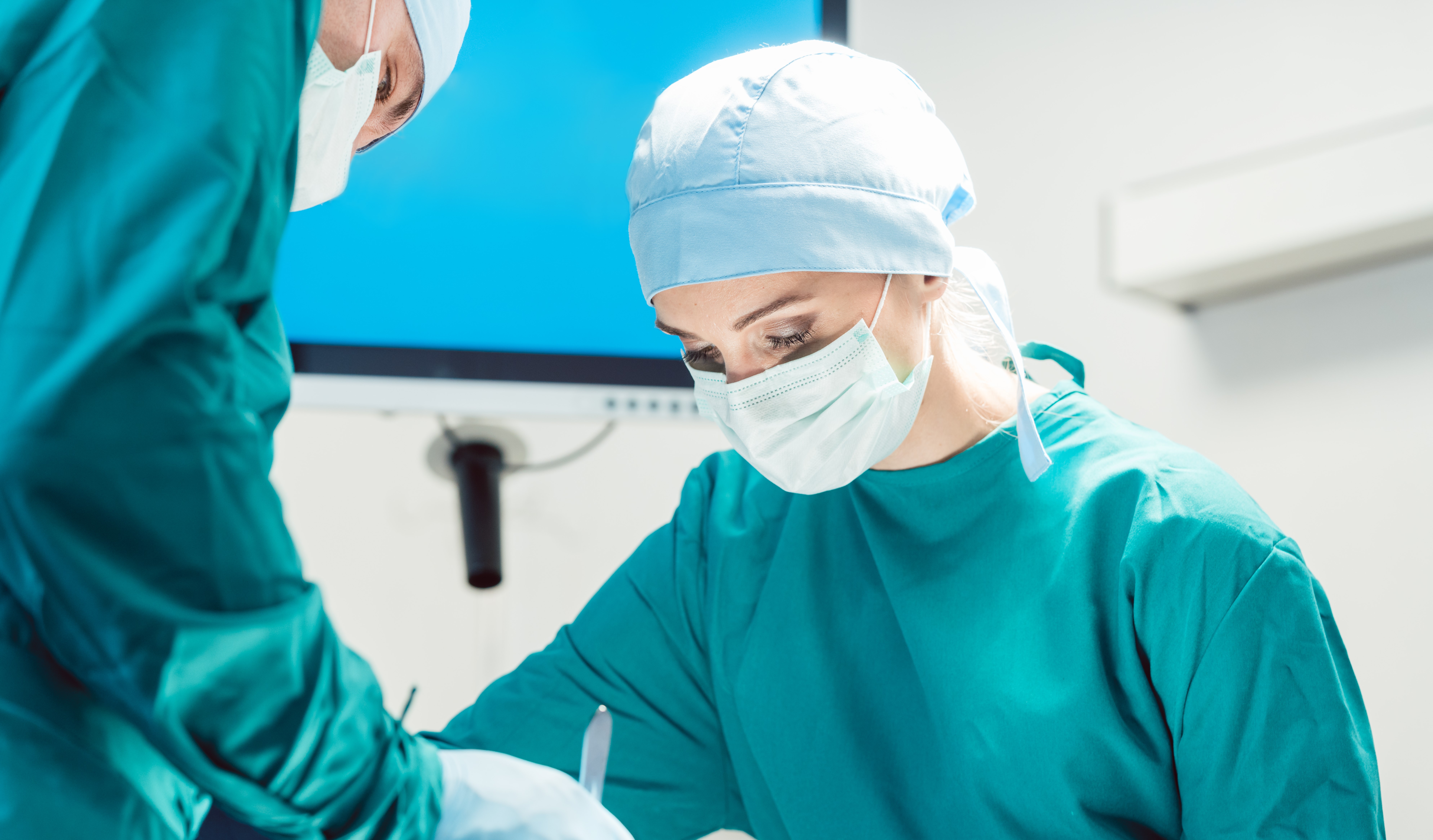 To personer i grønne klær og ansiktsmaske som utfører kirurgi