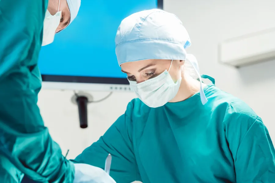 To personer i grønne klær og ansiktsmaske som utfører kirurgi