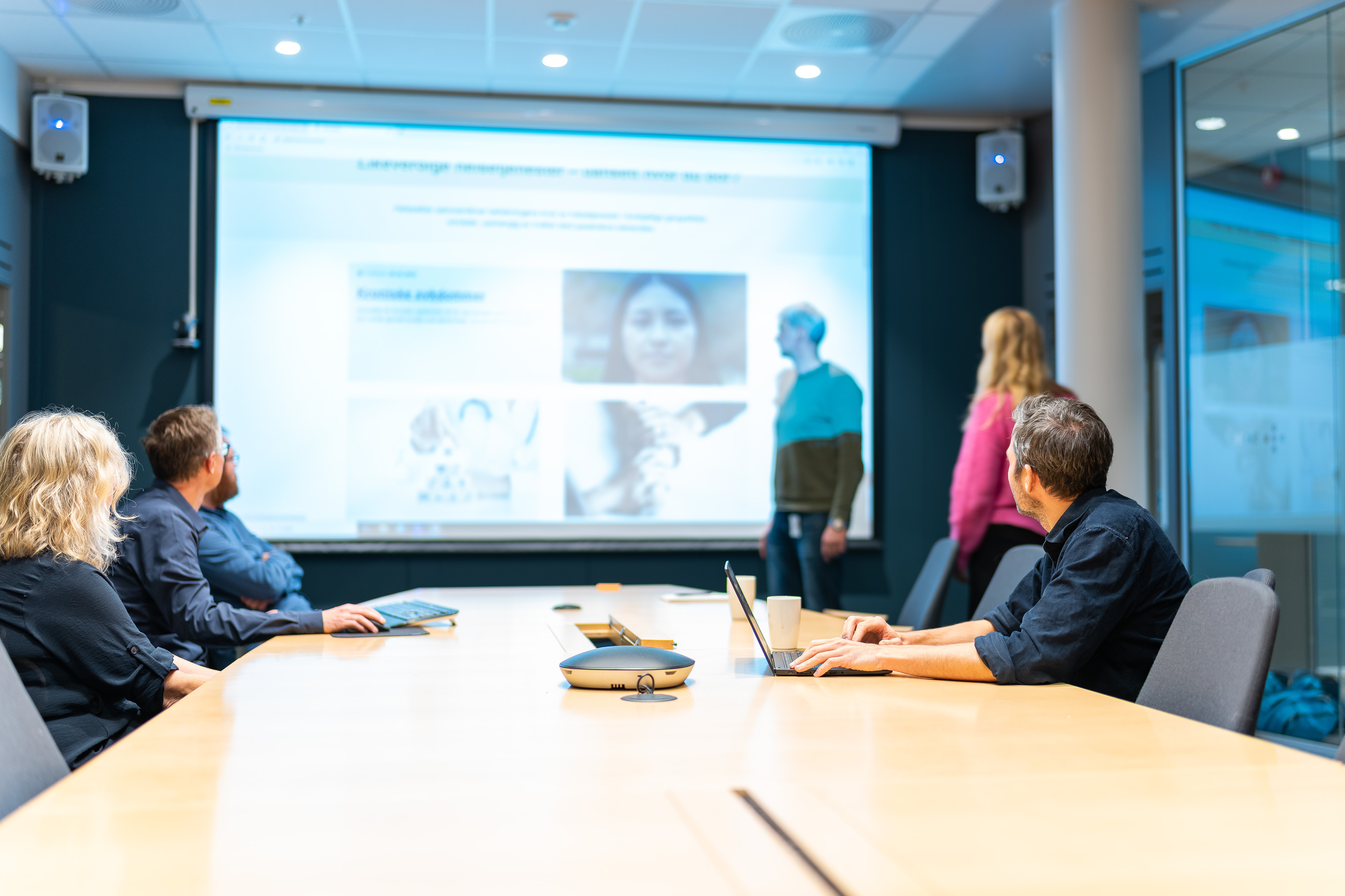 En gruppe mennesker som sitter ved et bord og ser på en projeksjonsskjerm