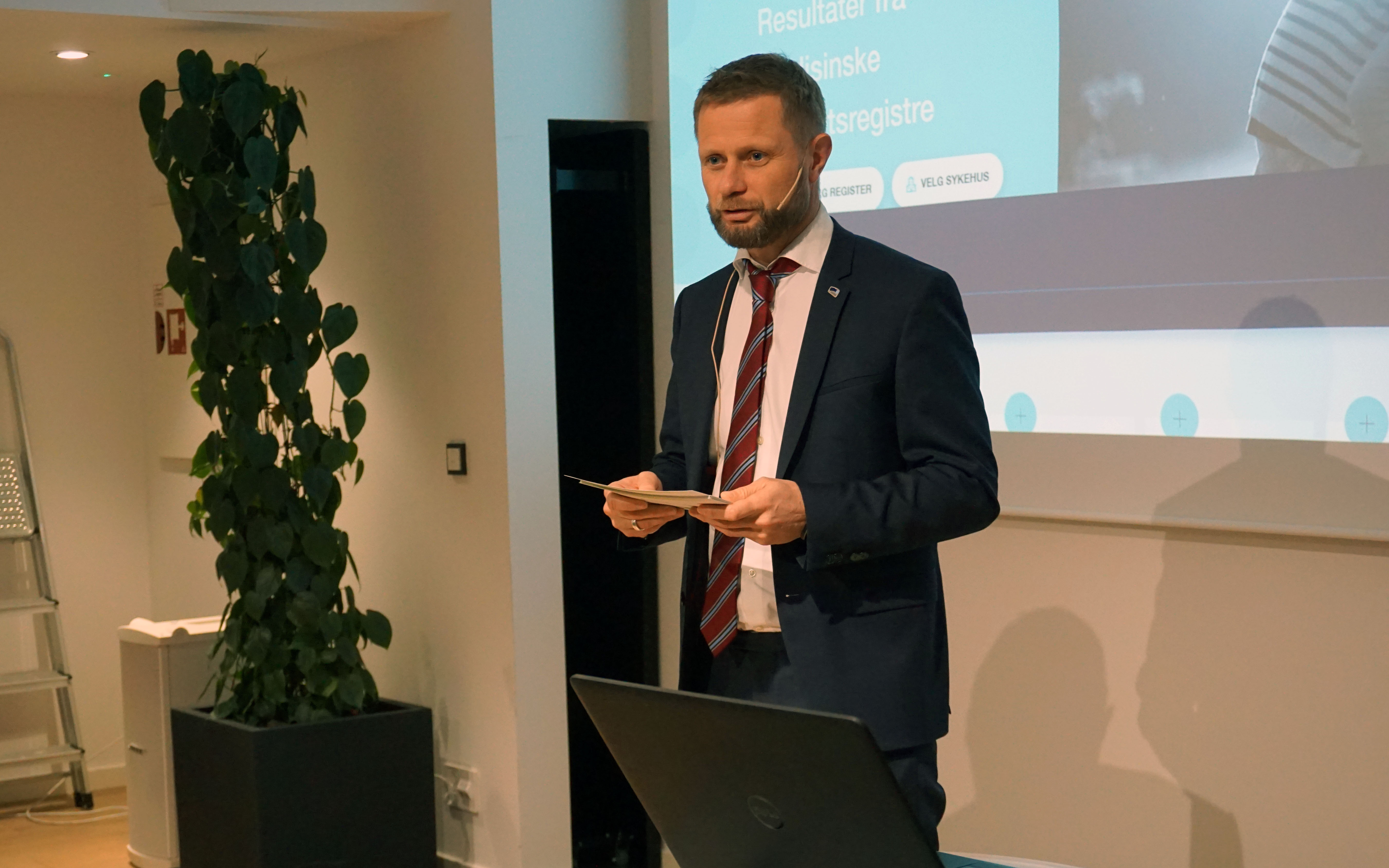 En mann i dress som holder en bok foran en projektorskjerm