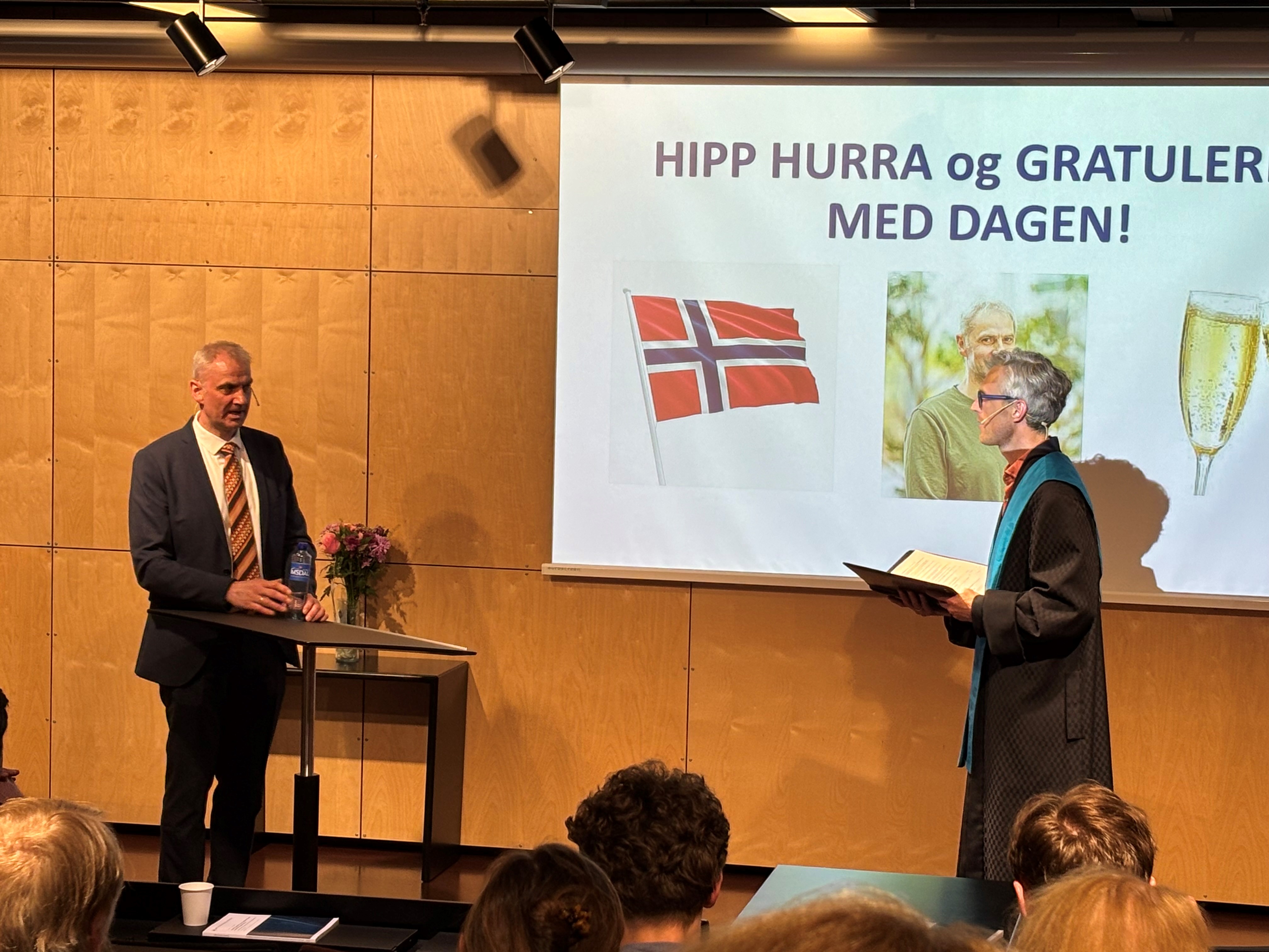 To menn på en scene foran en tavle